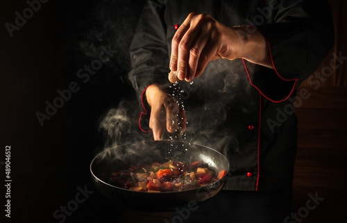Fototapeta Naklejka Na Ścianę i Meble -  Cooking fresh vegetables. The chef adds salt to a steaming hot pan. Grande cuisine idea for a hotel with advertising space