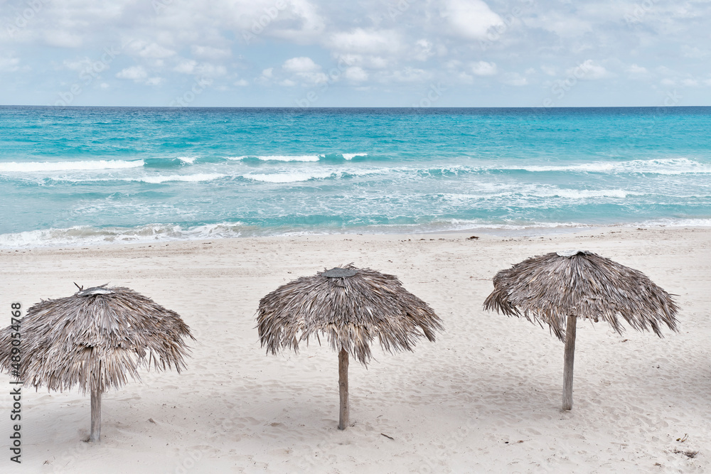 Atlantic sandy beach of Cuba, resort Varadero. Three palm leaf sun umbrellas.