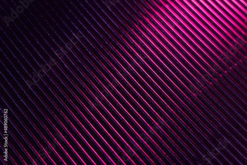 Corrugated texture. Neon light background. Grooved metal surface. Fluorescent pink purple color gradient glow reflection on parallel lines pattern dark black abstract overlay.