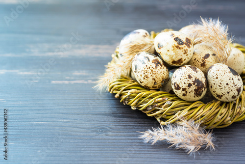 Quail eggs in the nest from willow branches and fluffy plaints on the wooden background. Minimal concept. Top view photo