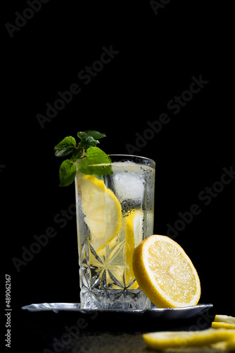 Un vaso de refrescante zumo de limón, cóctel de frutas con rodajas de limón y hielo sobre fondo negro	