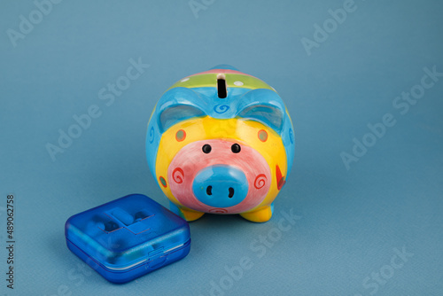 A piggy bank surrounded by pills on a blue background. the medicine. pills. the rise in price of medicines.