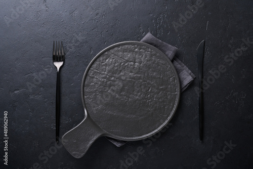 Black spoon, fork, knife and clean empty black plate. Set of stylish black and gold cutlery on black background. Fashionable and luxury eating. Top view. Copy space for your text.