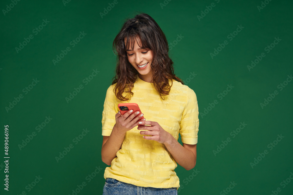 Smiling modern young girl hold phone looking at smartphone using mobile dating apps, chatting online on green background
