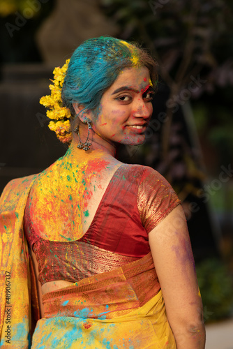 Young beautiful girl or woman or lady in indian attire saree looking back with dry organic color or colour or gulal or abeer or Holi powder on her face, Festival of color holi
