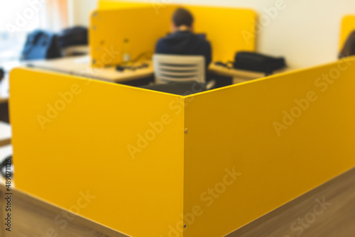 View of modern office space interior with desks in yellow tones with workers, employee with a laptop on a cozy workplace in the background, it-company open space with tables, chairs and rooms