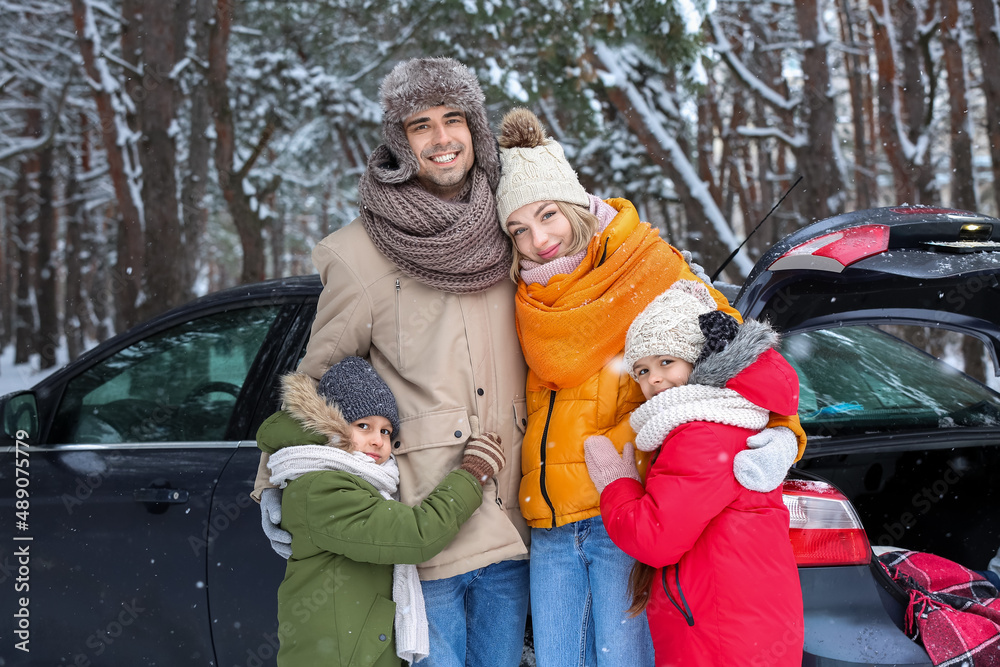 Happy family hugging near car in forest on snowy winter day