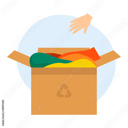 Cardboard box with old clothes for recycling and donating. The hand throws the clothes into the box