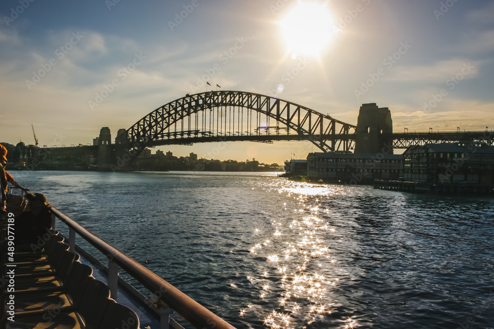 View of Sydney Harbor Bridge with sun setting behind it; view from a ship