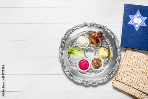 Passover Seder plate with traditional food, matza and Torah on white wooden background