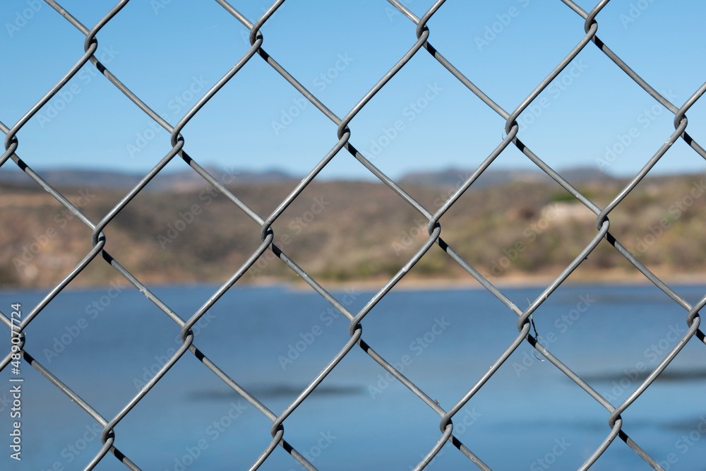 Close-up Of Chainlink Fence Against Lake and a hill Close-up Of Chainlink Fence Against Lake and a hill
