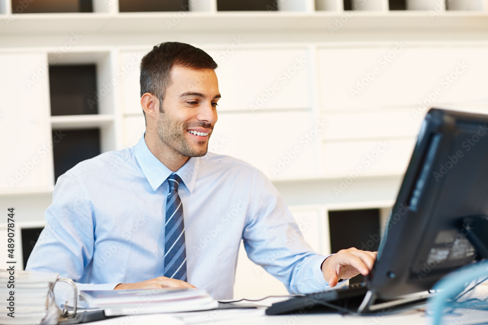 Fototapeta premium Ive got new client emails. A positive young businessman working at his desk in front of his computer.