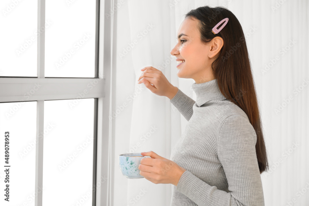 Morning of pretty young woman drinking tea near window