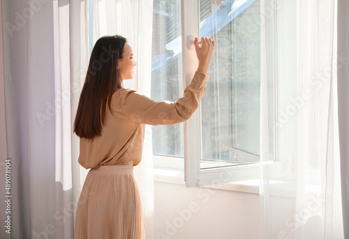 Pretty young woman opening window in room