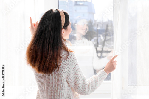 Pretty young Asian woman opening curtains in room © Pixel-Shot
