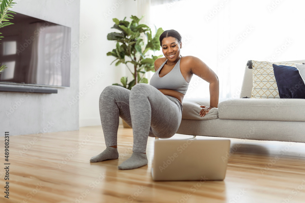 African american woman working out in home livingroom gym with laptop African american woman working out in home livingroom gym with laptop