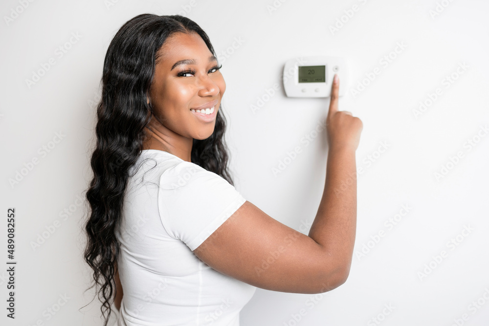 African woman lady adjusting the climate control panel on the wall wall thermostat African woman lady adjusting the climate control panel on the wall wall thermostat