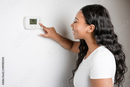 African woman lady adjusting the climate control panel on the wall wall thermostat