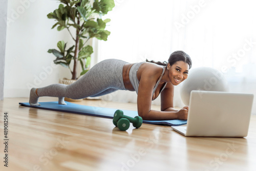 African american woman working out abdo in home livingroom gym with laptop photo