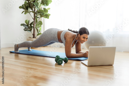 African american woman working out abdo in home livingroom gym with laptop photo