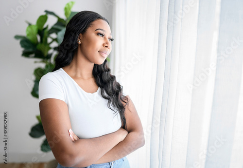 African American woman looking to aside out window, standing at home
