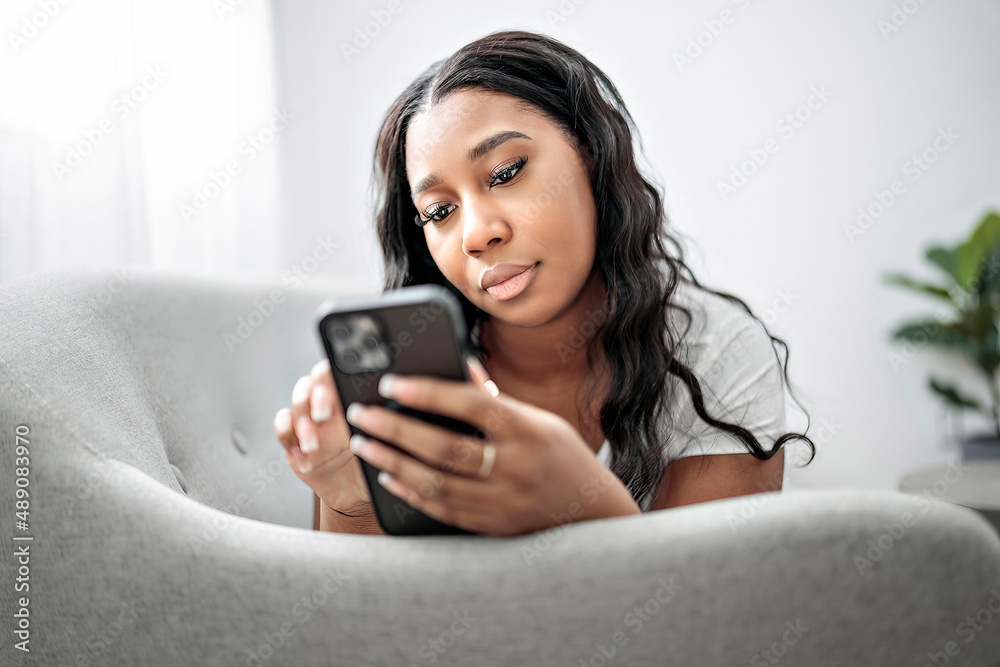 Attractive young African woman sitting on the couch at home with cellphone Attractive young African woman sitting on the couch at home with cellphone