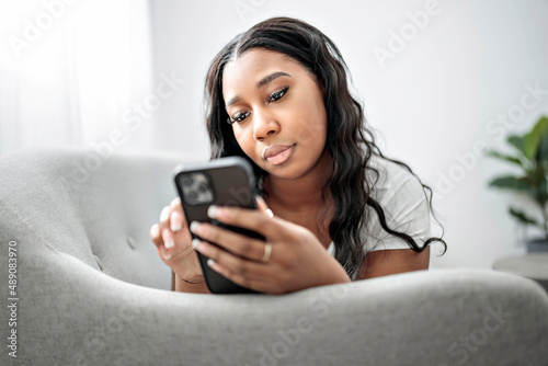 Attractive young African woman sitting on the couch at home with cellphone
