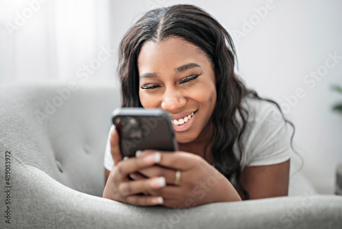 Attractive young African woman sitting on the couch at home with cellphone