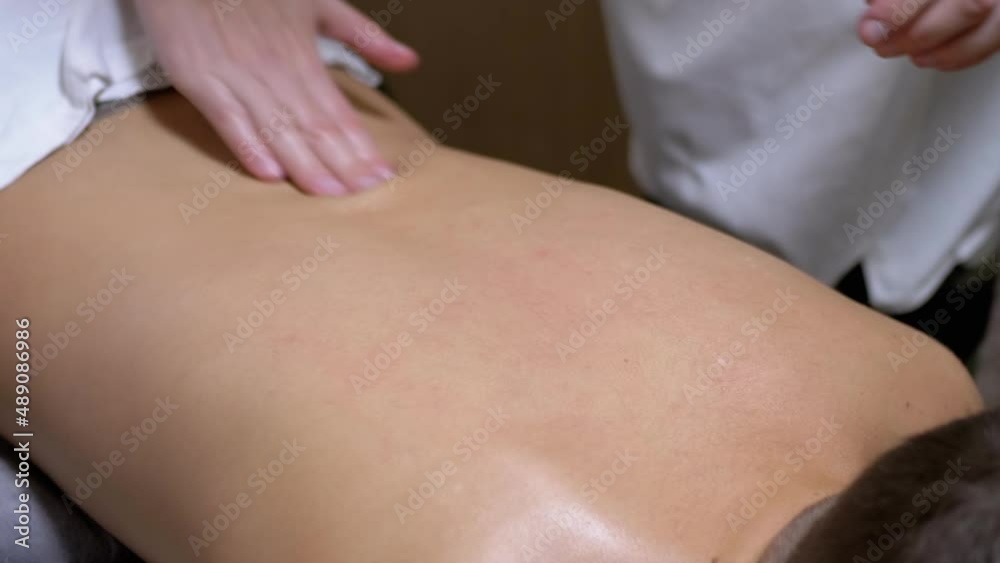 Hands of the Masseur are Massaging Back of a Teenager, a Child in a Spa Salon. Therapeutic, preventive massage session using oil. Eliminating pain, relaxing muscles, improving blood circulation. Zoom. Hands of the Masseur are Massaging Back of a Teenager, a Child in a Spa Salon. Therapeutic, preventive massage session using oil. Eliminating pain, relaxing muscles, improving blood circulation. Zoom.