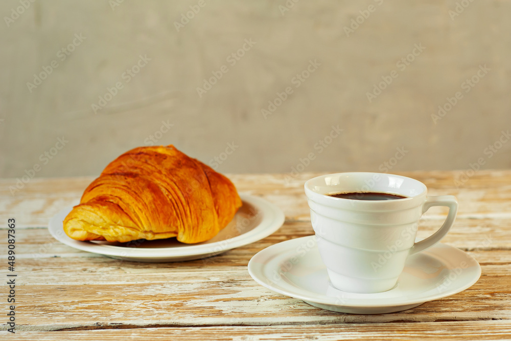 Coffee in a white ceramic mug. Croissant with coffee for breakfast. Coffee on an old wooden table. Coffee in a white ceramic mug. Croissant with coffee for breakfast. Coffee on an old wooden table.