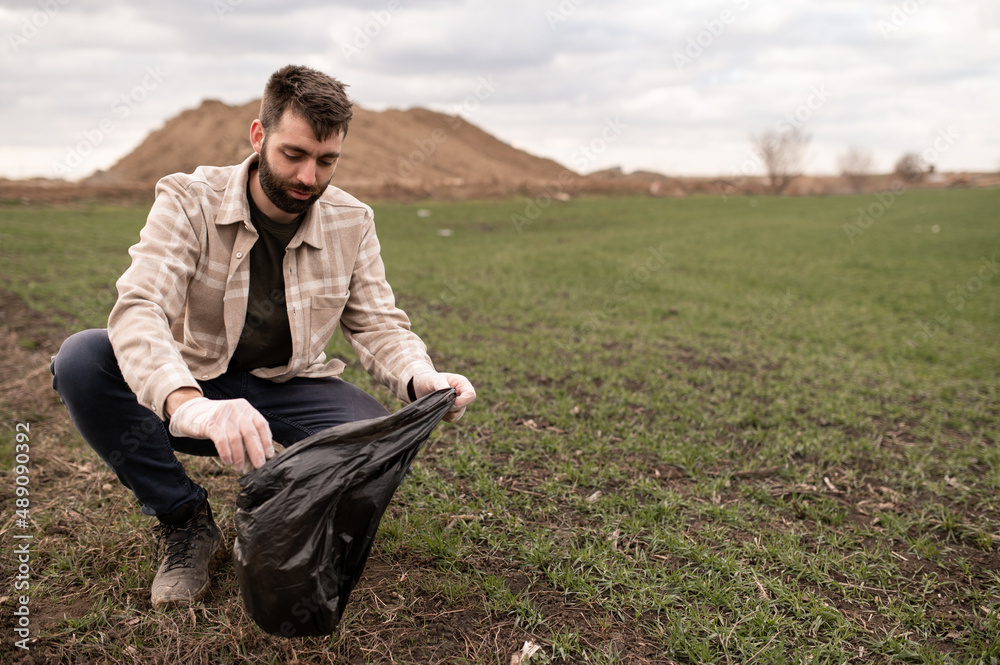 Young farmer collecting garbage at his field and also inspecting the land. Protect the nature concept. Young farmer collecting garbage at his field and also inspecting the land. Protect the nature concept.