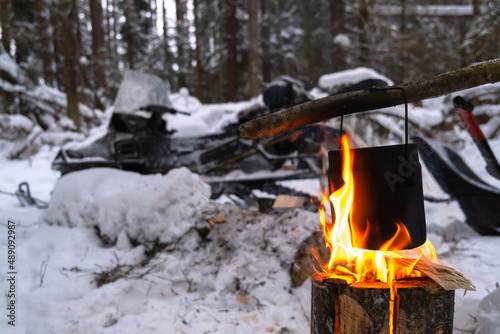 kettle is heated on fire. Finnish candle on the background of snowmobile. concept of relaxing in the forest in winter