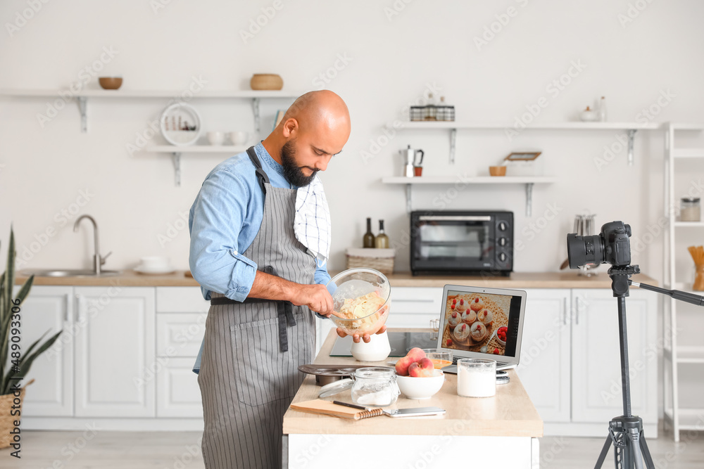 Handsome man preparing peach muffins and recording video tutorial in kitchen Handsome man preparing peach muffins and recording video tutorial in kitchen