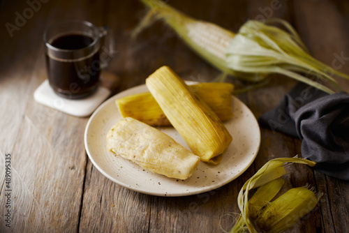 Humitas are savory steamed fresh corn cakes, a traditional Ecuadorian appetizer. It’s accompanied by coffee, on a wooden background.  photo
