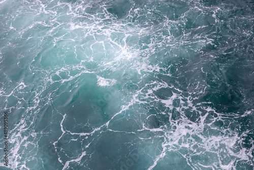 Water surface abstract background. White waves and foam on the blue sea water. Wake behind ship