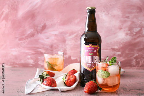 Bottle and glass of fresh iced strawberry kombucha on pink background