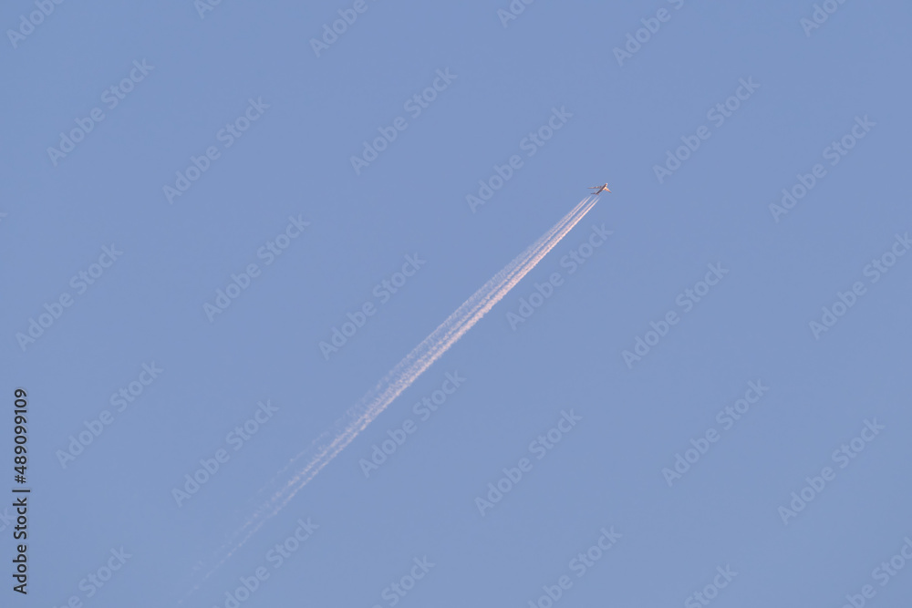 Distant passenger jet plane flying on high altitude on clear blue sky leaving white smoke trace of contrail behind. Air transportation concept Distant passenger jet plane flying on high altitude on clear blue sky leaving white smoke trace of contrail behind. Air transportation concept
