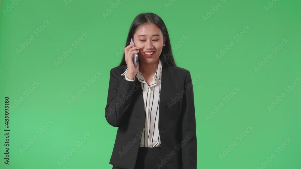 A Smiling Asian Business Woman Talking On Mobile Phone While Walking In Front Of Green Screen In The Studio
A Smiling Asian Business Woman Talking On Mobile Phone While Walking In Front Of Green Screen In The Studio