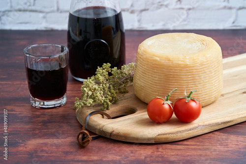 Italian hard cheeses such as pecorino or caprino, Italian wine with carafe and traditional glass, two tomatoes and oregano. A bunch of oregano on a wooden board. 