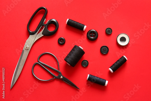 Thread spools with buttons and scissors on red background