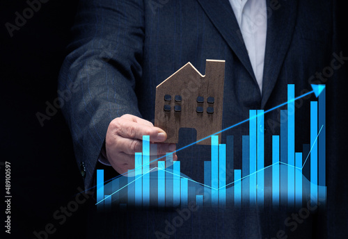 hand holds a wooden model of a house on a dark background. Real estate sale and purchase concept, rise in property prices