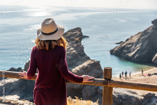 A young tourist girl with a hat looking at the beautiful Cala Peñon cut off a virgin and hidden beach in Almería. Mediterranean sea on the coast. Almanzora Caves, Almería