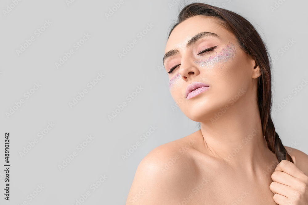 Beautiful young woman with glitters on her face against light background Beautiful young woman with glitters on her face against light background