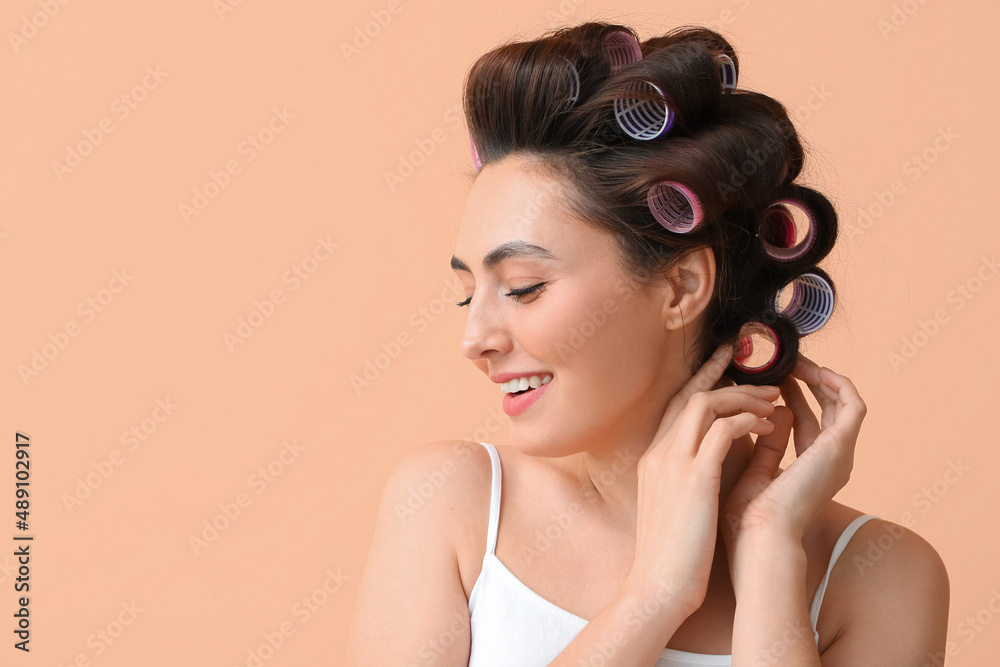 Fototapeta premium Beautiful young woman in hair rollers on color background