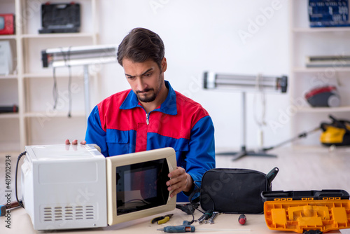 Young male repairman repairing oven at workshop