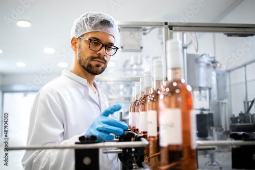 Technologist in white clothing and hairnet controlling production of beverage in wine bottling factory.