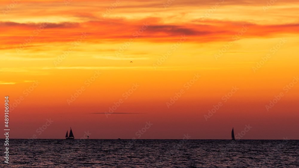 sailboats in silhouette on horizon against vibrant sky