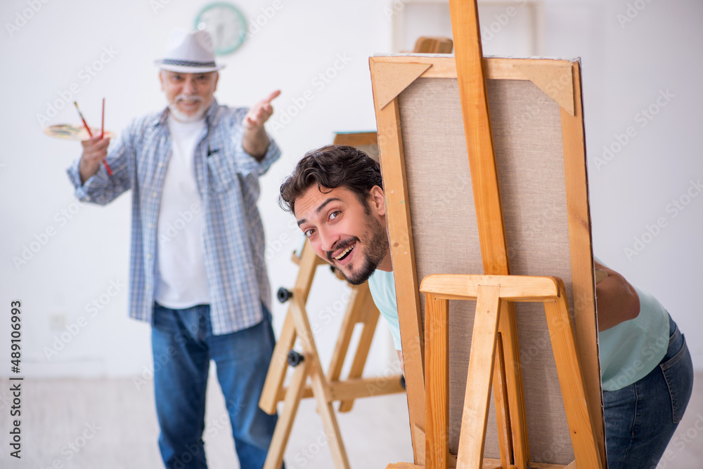 Old painter teaching young student at studio