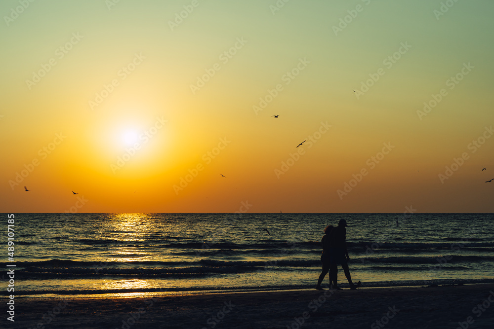People walking along the beach in silhouette at sunset
