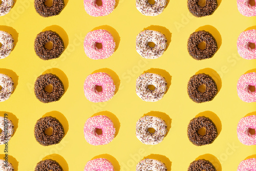 Arranged small ring donuts with white, pink and chocolate glaze. Colorful crumbs on a yellow pastel background. Pattern. Flat lay.